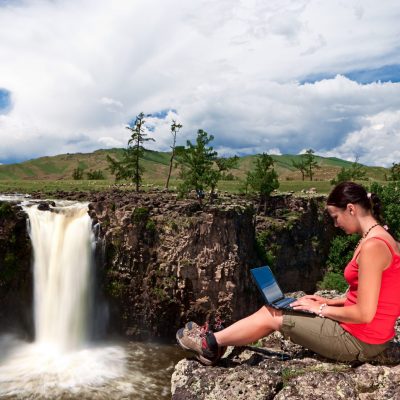 A young womanl sitting on a rock and using laptop. Waterfall on the background.http://bem.2be.pl/IS/outdoors_laptop_380.jpg